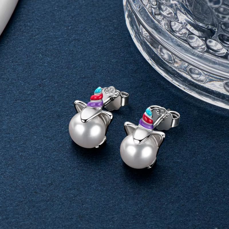 Boucle D'oreille Licorne Perle, présentée sur un tissu bleu foncé