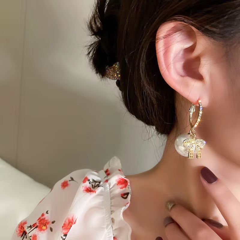Boucle D'oreille Originale Femme Boule de Noël et Nœud, portée par une femme de profil pour qu'on voie bien la boucle d'oreille, on ne voit pas son visage.