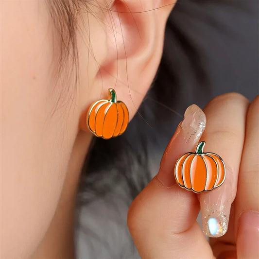 Boucle d’oreille originale femme citrouille Halloween, porté sur une oreille et l'autre boucle entre ses doigts présentée à côté.