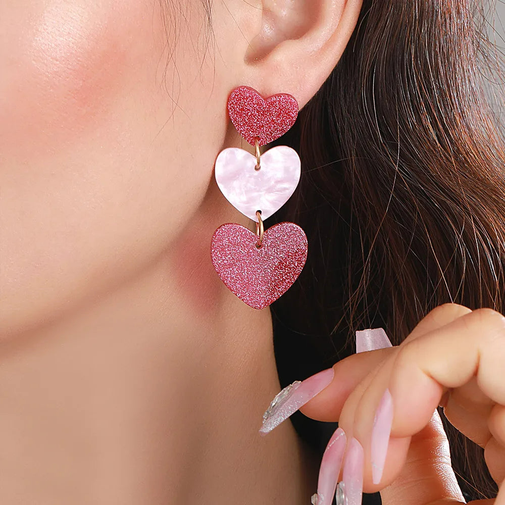 Boucle D'oreille Originale Femme Pendante 3 Cœurs, portée par une femme, on ne voit que le bas de sa joue, son oreille et ses cheveux derrière. Image