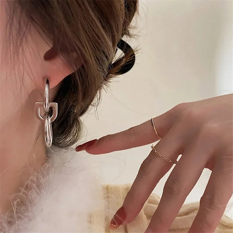 Boucle d'Oreille Pendante Argentée Géométrique Et Moderne porté par une mannequin qui la montre du doigt. Image