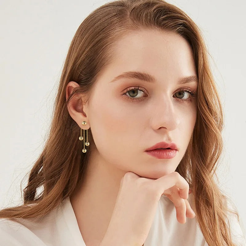 Boucle D'oreille Pendante Doré Élégante, porté par une mannequin quipose avec la main sous lemaenton.