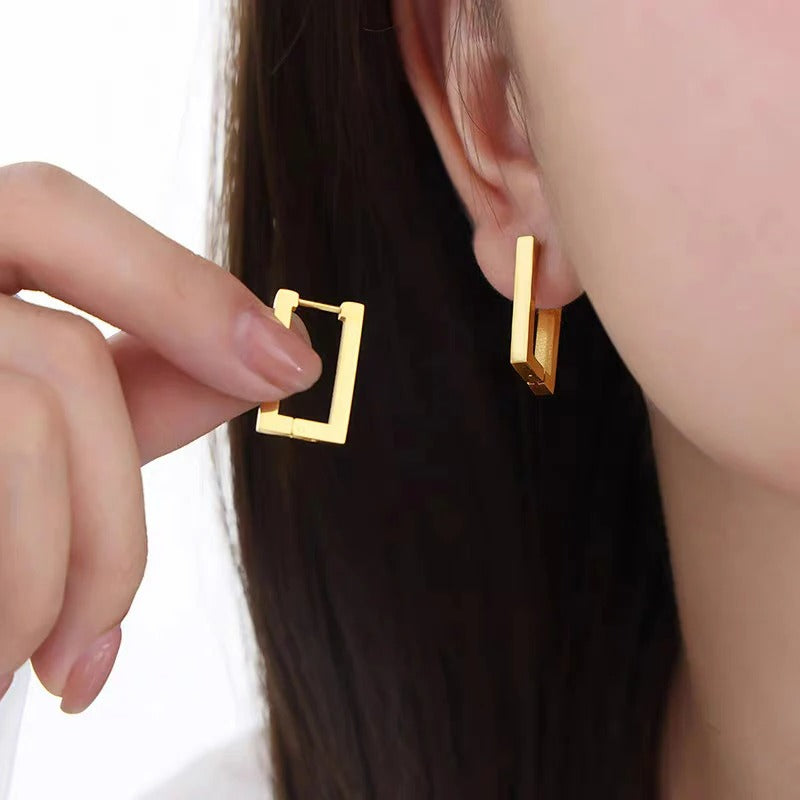 Boucle D'oreille Rectangulaire Doré Acier Inoxydable portée par une femme qui montre l'autre boucle entre ses doigts à côté