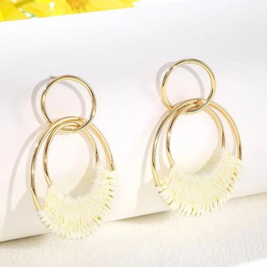 Paire de boucle d'oreille bohème chic ronde, avec fantaisie tressage au fil blanc pour relier deux anneaux, les boucles sont sur un présentoir blanc. .