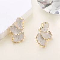 Boucle D'oreille Fleur Irrégulière Nacrée dorée et blanche nacrée, posé sur un fond beige.