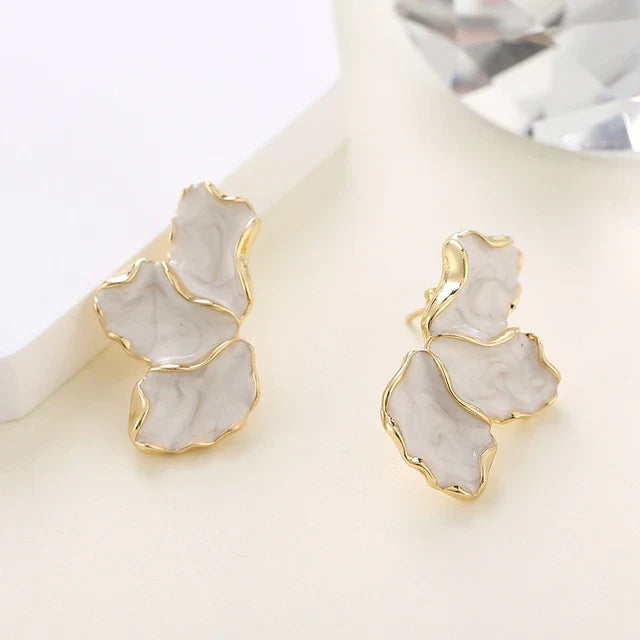 Boucle D'oreille Fleur Irrégulière Nacrée dorée et blanche nacrée, posé sur un fond beige. Image