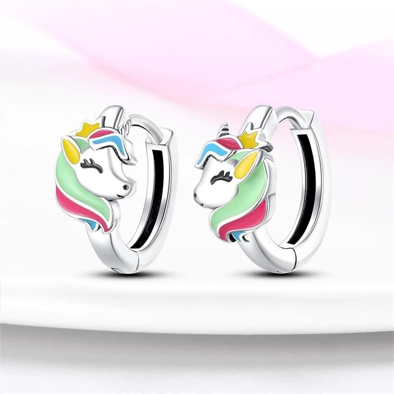 Boucle D'oreille Licorne Créole Argentée, la paire est présenté sur un fond blanc avec un ruban rose dans le fond.