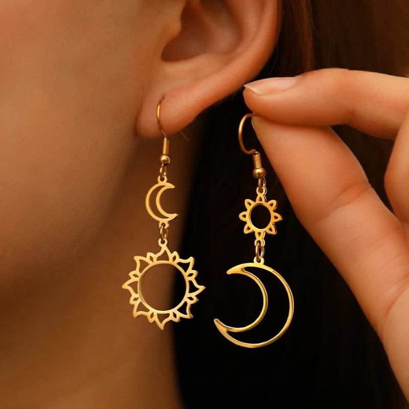 Boucle D'oreille Lune et Soleil Doré Pendante, portée par une mannequin, une boucle à l'oreille, l'autre boucle dans les doigts, qu'elle présente à côté.