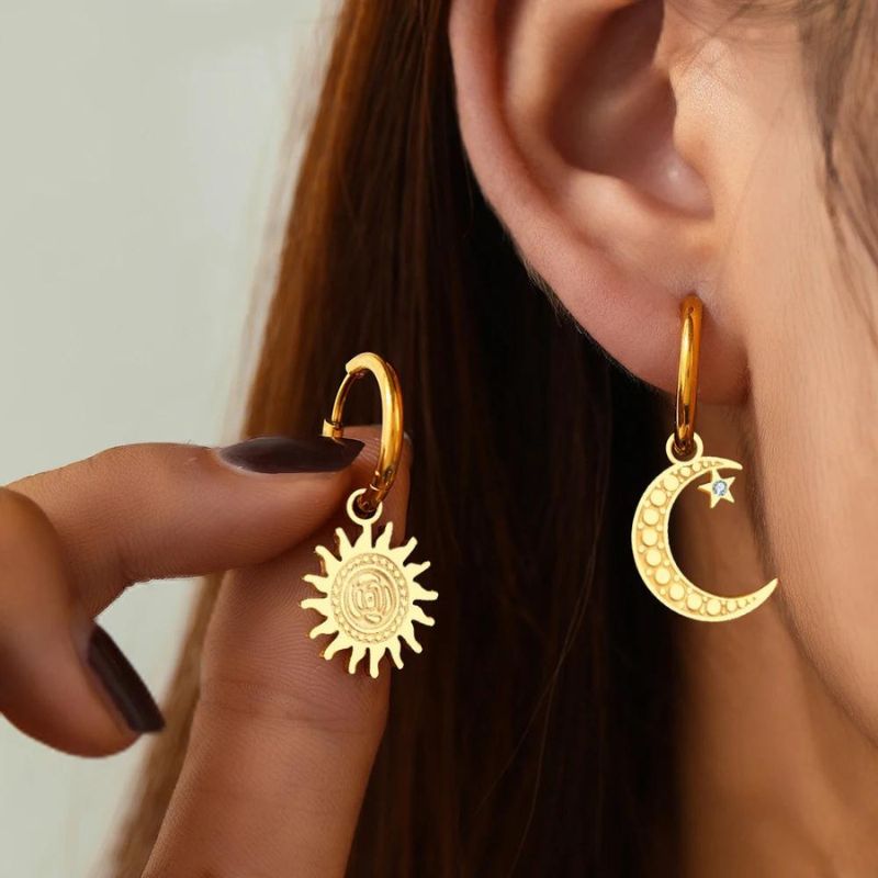 Boucle D'oreille Lune et Soleil Versatile, portée par une mannequin, elle présente la boucle avec le soleil dans ses doigts à côté de la boucle lune à son oreille.