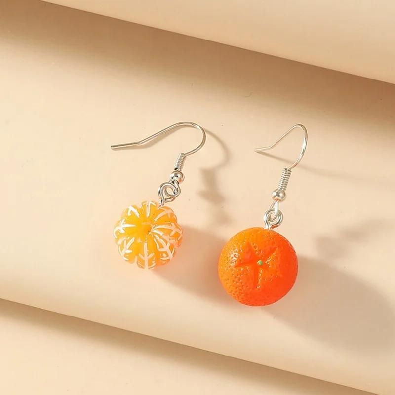 Boucle D'oreille Orange Fruit Dépareillée, une mini orange avec la peau, l'autre sans la peau. sur un socle beige. Image