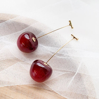 Boucle d'Oreille Rouge Élégante en Forme de Cerise posée sur un tissu blanc