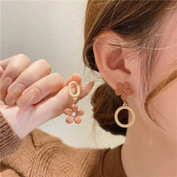 Boucles D'oreilles Asymétriques Fleur Mat, portés par une femme, elle présente l'autre boucle entre ses doigts à côté de celle à son oreille.