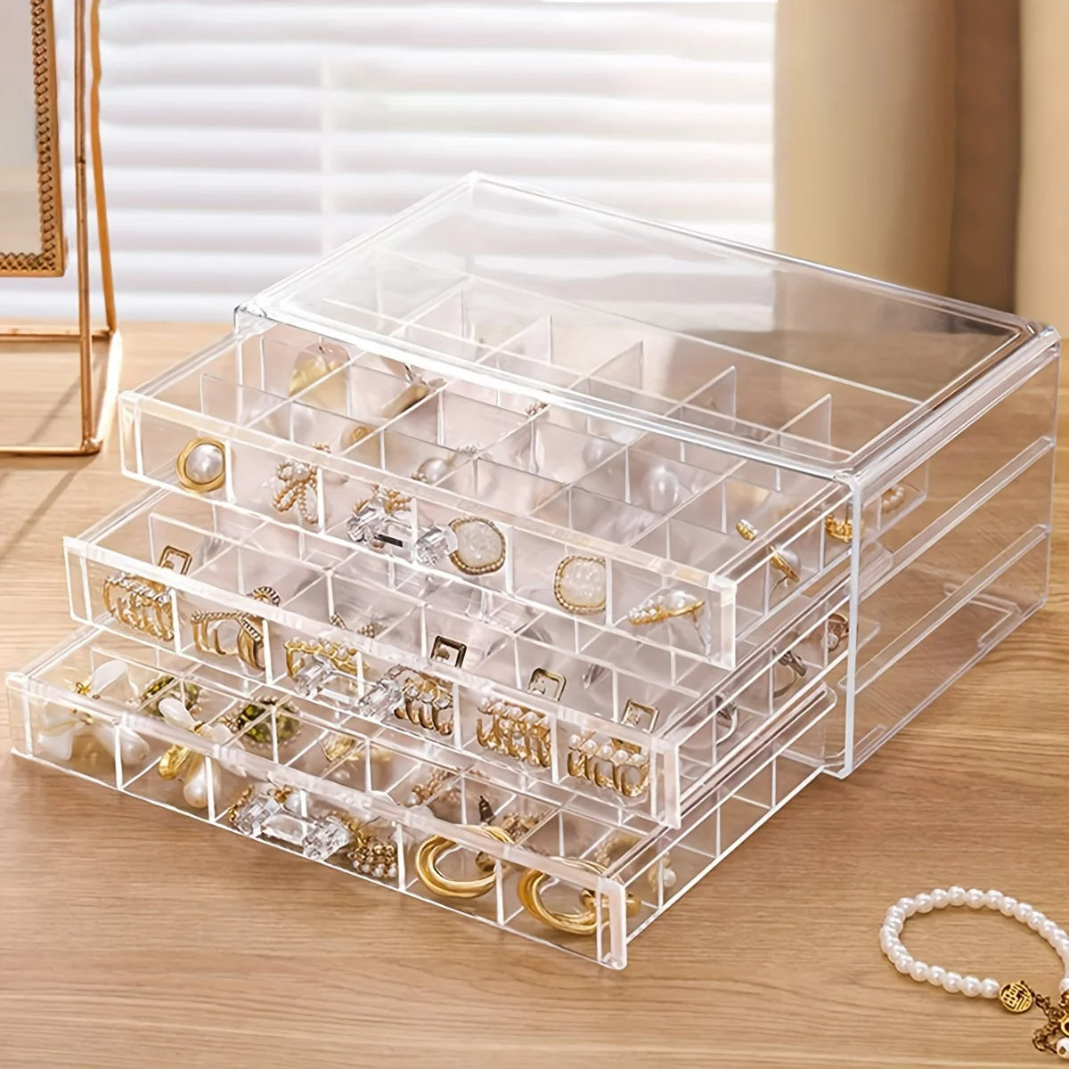 Rangement Boucle D'oreille 3 Tiroirs blanc transparent, ouvert avec des bijoux à l'intérieur, posé sur une commode en bois. Image